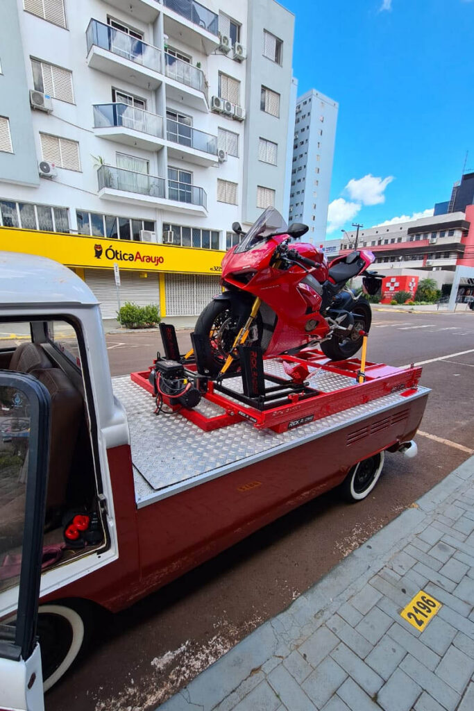 Red motorcycle on a red platform at the rear of a vehicle parked on a street