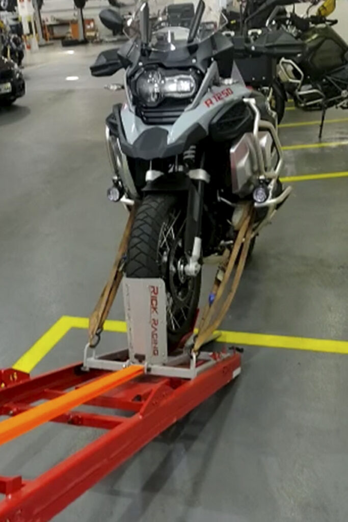 Adventure motorcycle strapped to a red ramp indoors